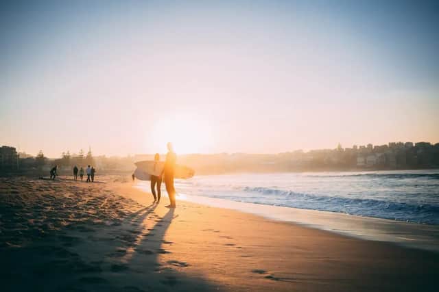 Deux surfeurs en silhouette, planches à la main, se tiennent sur une plage de sable, contemplant l'océan lors d'un coucher de soleil doré.