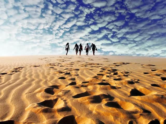 Un grupo de WeRoad camina por una inmensa duna de arena, dejando huellas en la arena bajo un cielo azul nublado.