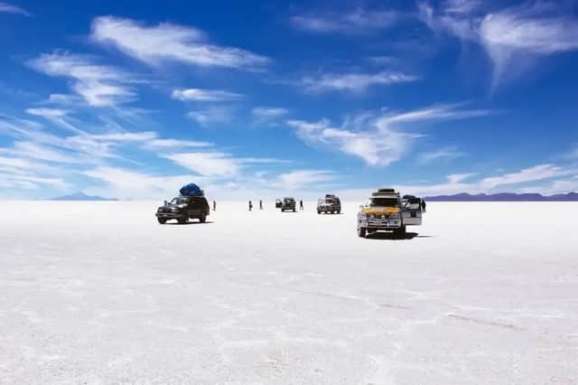 Eine WeRoad-Gruppenreise mit mehreren Geländefahrzeugen stoppte auf einer riesigen, weißen Salzebene unter einem strahlend blauen Himmel mit zarten Wolken.