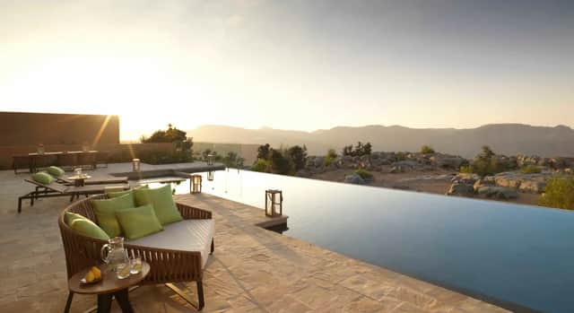 A modern patio with an infinity pool and lounge furniture overlooking a rocky mountain landscape at sunset.