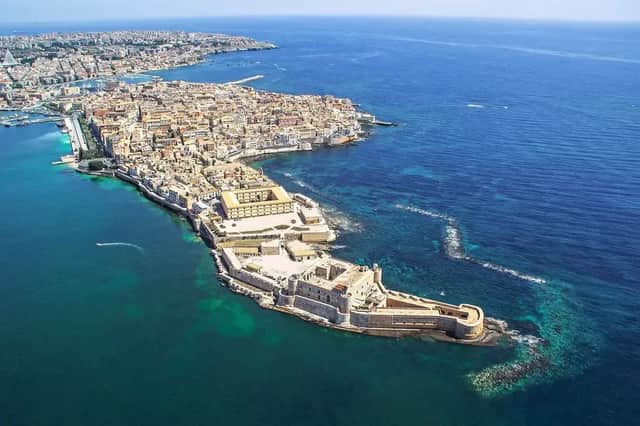Une vue aérienne d'une ville côtière historique et d'une forteresse sur une péninsule, entourée d'une mer turquoise et d'un bleu profond.