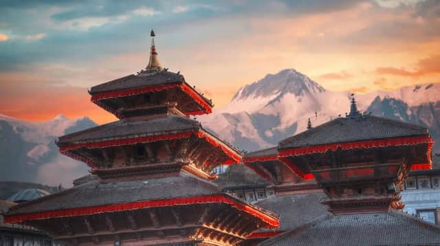 Mehrstufige Pagodendächer mit roter Zierleiste stehen vor schneebedeckten Bergen unter einem farbenfrohen Sonnenuntergangshimmel.
