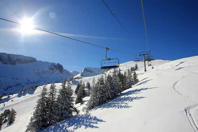 Un telesilla vacío asciende por una ladera de montaña cubierta de nieve, rodeada de pinos en un día soleado.