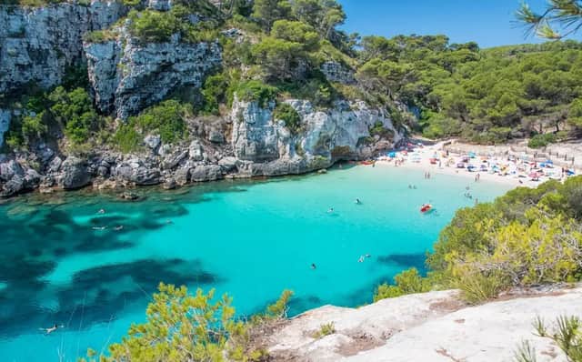 Luftaufnahme einer Bucht mit Menschen, die in klarem türkisfarbenem Wasser schwimmen und an einem weißen Sandstrand entspannen, umgeben von felsigen Klippen und Bäumen.