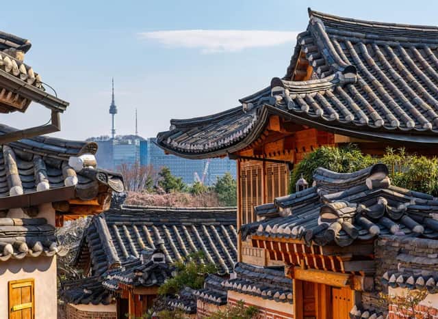 Una vista sobre tejados tradicionales coreanos con un horizonte moderno de la ciudad y una torre de comunicaciones visible en la distancia.