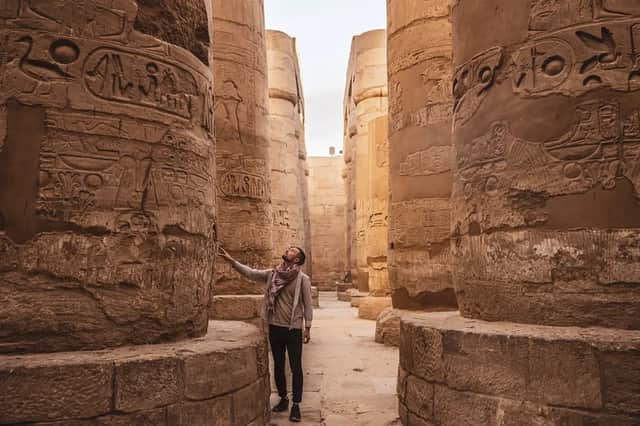 A man stands in an ancient temple hall, looking up at the hieroglyphs carved into the massive stone columns.