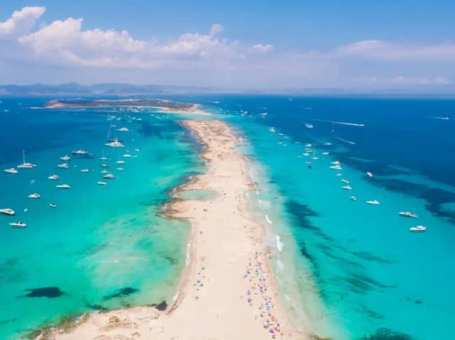 Una vista aerea di una lunga lingua di sabbia che si estende in un mare turchese, con molte barche ancorate e persone sulla spiaggia.