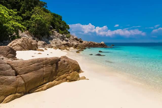 Una spiaggia isolata di sabbia bianca con grandi rocce lambisce acque cristalline turchesi sotto un cielo azzurro.