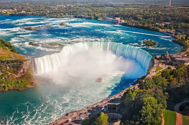 Luftaufnahme eines riesigen, hufeisenförmigen Wasserfalls, an dessen Basis ein Touristenboot durch die nebligen Gewässer fährt.