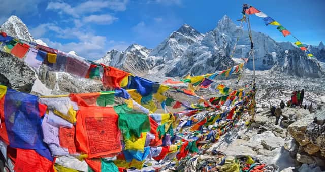 Banderas de oración de colores se extendían por un mirador rocoso, con montañas nevadas y un glaciar al fondo bajo un cielo azul.
