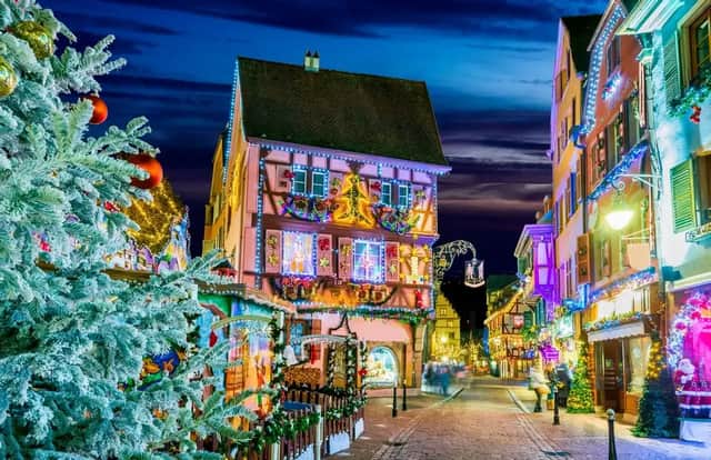 Una calle estrecha de adoquines por la noche, con edificios de entramado de madera y un gran árbol de Navidad cubierto de luces festivas.