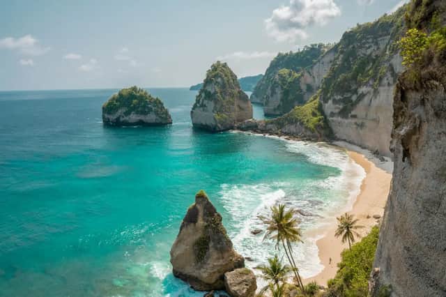 Una spiaggia sabbiosa appartata con palme, circondata da scogliere ripide e acqua turchese con grandi formazioni rocciose.