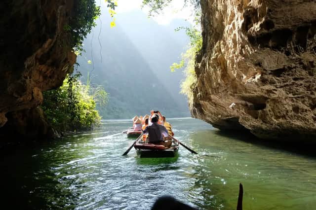 Un viaje en grupo de WeRoad rema en botes por un río a través de un desfiladero soleado entre grandes acantilados rocosos.