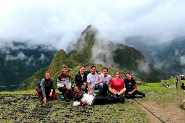 Un viaje en grupo de WeRoad posa para una foto en un mirador cubierto de hierba, con montañas cubiertas de niebla al fondo.