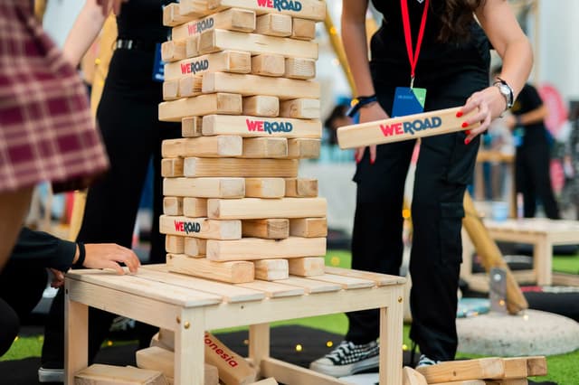 Personas jugando a una torre gigante de bloques de madera con el logo de WeRoad en un evento.