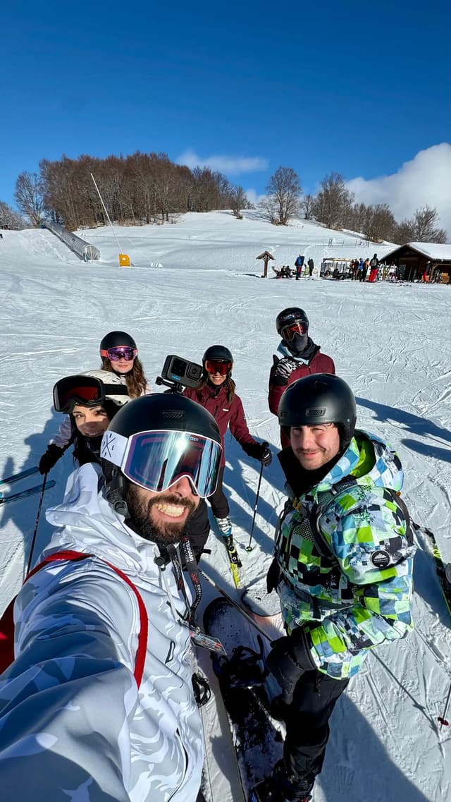 Un viaje en grupo de WeRoad posando para un selfi en una pista de esquí nevada con cascos y gafas bajo un cielo soleado
