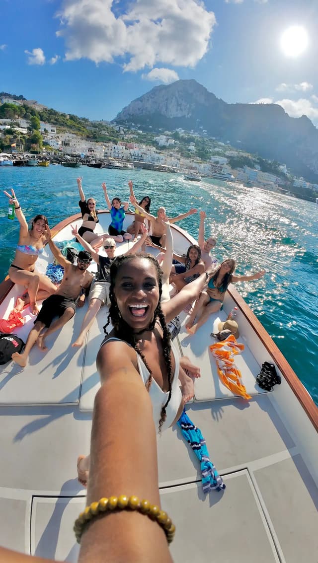 Un groupe WeRoad prend un selfie souriant sur un bateau, avec une côte montagneuse en arrière-plan sous un ciel ensoleillé.