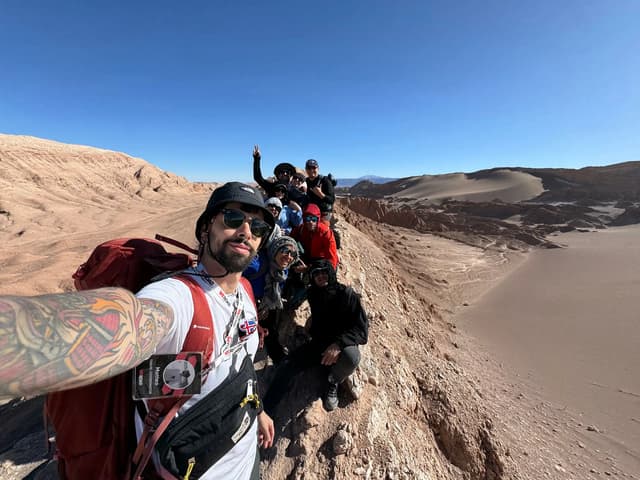 Groupe de voyageurs WeRoad en selfie panoramique sur la crête rocheuse de la Vallée de la Lune, désert d'Atacama, Chili, avec dunes de sable et montagnes en arrière-plan