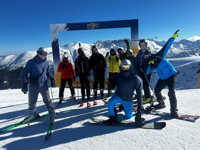 Un voyage de groupe WeRoad posant avec des skis et des snowboards devant un cadre photo sur un sommet enneigé.