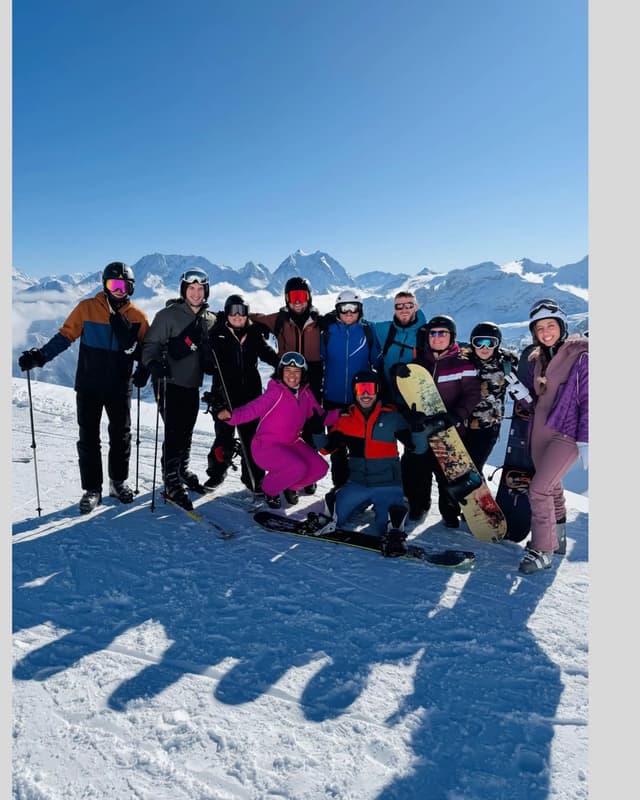 Un viaggio di gruppo WeRoad di sciatori e snowboarder in posa insieme sulla cima di una montagna innevata sotto un cielo azzurro e limpido