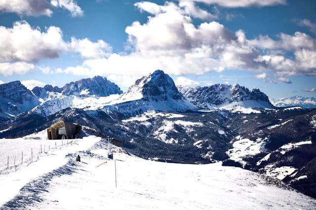 Snow-capped peaks and ski slopes under a blue sky with clouds.