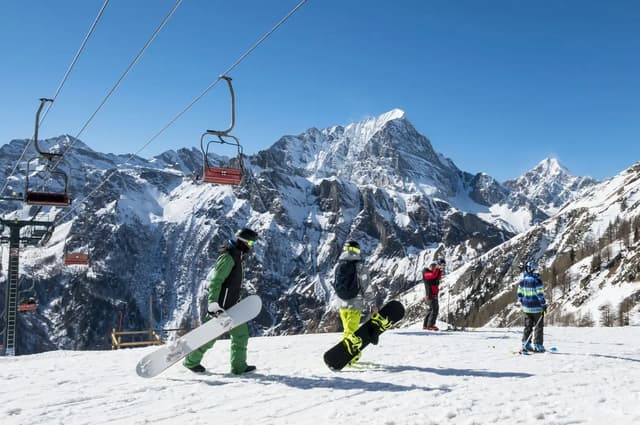 Snowboarders on a snowy slope next to a chairlift with mountains behind.