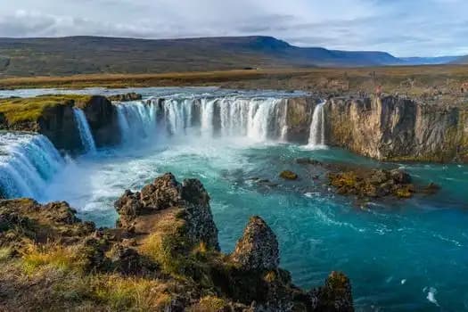 Breiter Wasserfall in einer Schlucht mit türkisfarbenem Wasser, Island