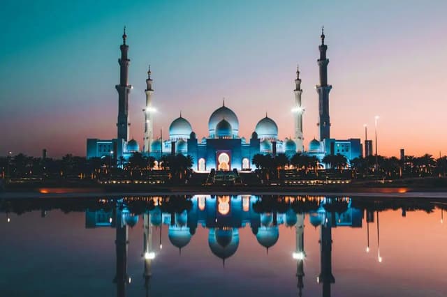 Gran Mezquita Sheikh Zayed iluminada al anochecer y reflejada en el agua, Abu Dabi