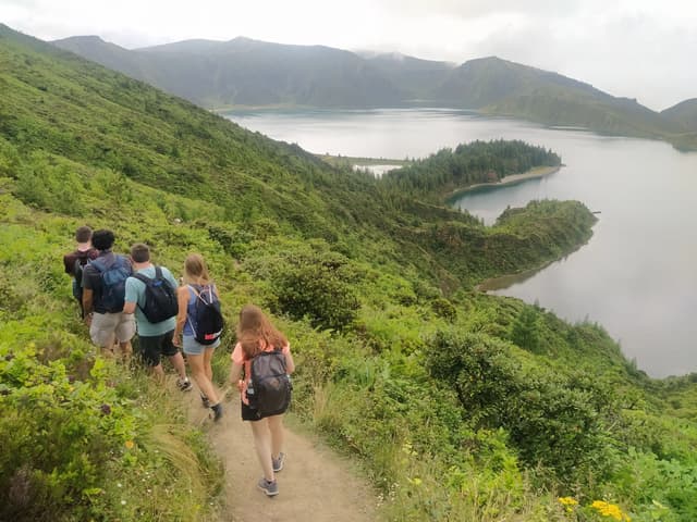 Un grupo de senderistas camina por un sendero verde con vistas a un lago de cráter.