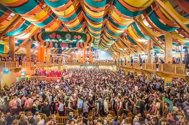 Interior de una gran carpa del Oktoberfest de Múnich llena de gente bajo un techo de telas de colores.