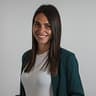 Donna con lunghi capelli scuri, blazer verde scuro su top bianco, sorride in un ritratto.